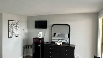 Une chambre à coucher comprenant un lit, une commode, un téléviseur, une machine à café et une poubelle.