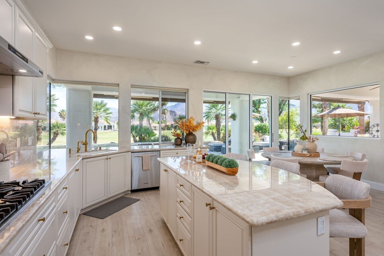 A modern kitchen with a large island, white cabinetry, and a view of a landscaped outdoor area.