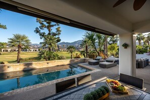 A poolside area with a view of a golf course and mountains, outdoor furniture, and a fruit basket. - Casa Caliza at PGA West | Nicklaus Fairway Views (La Quinta)