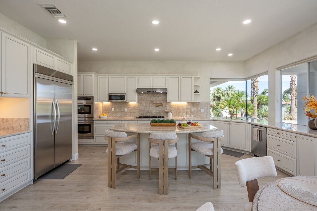 A modern kitchen with a central island, stainless steel appliances, and a view of palm trees.
