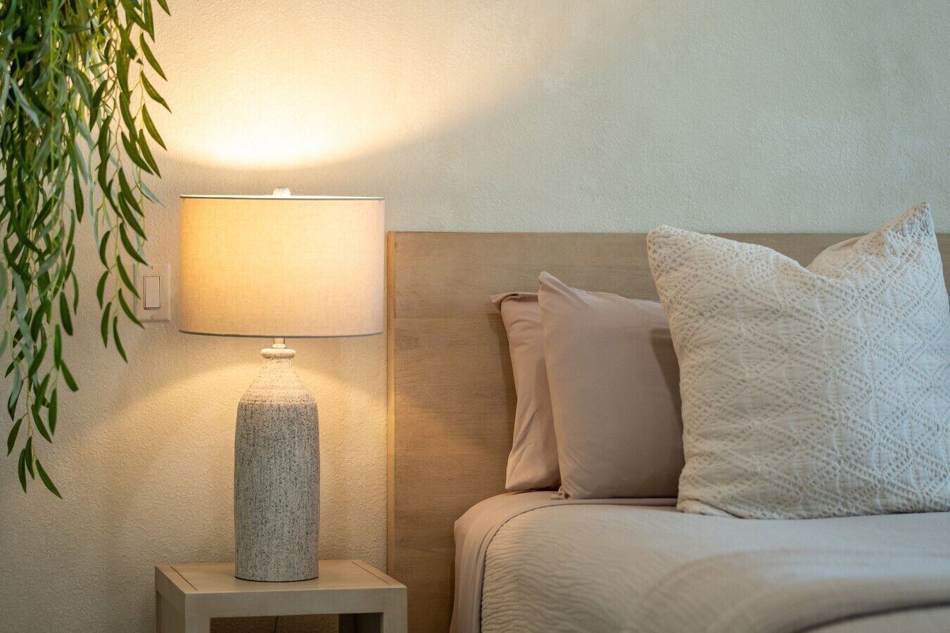 A neatly made bed with a headboard, a bedside lamp, and a wall-mounted switch.