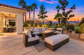 An outdoor patio with wicker furniture, a fire pit, and umbrellas. - Solmirage at PGA West | Nicklaus Fairway Views (La Quinta)
