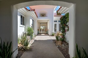 A pathway leading to a house with a covered entrance, white walls, and a tiled roof. - Casa Caliza at PGA West | Nicklaus Fairway Views (La Quinta)