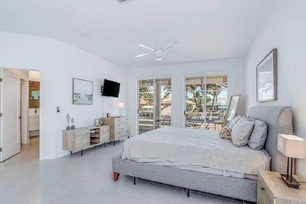 Un dormitorio moderno con una cama grande, un televisor, un ventilador de techo y un balcón con mobiliario exterior.