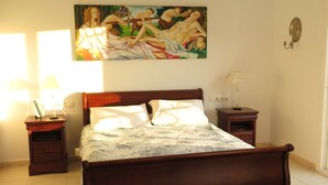 A bedroom with a wooden bed, a nightstand, a lamp, a painting on the wall, and a patterned rug. - Villa La Malcontenta, large private house with green spaces and swimming pool. (Alcaucín)