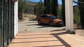 A covered driveway leading to a parked car, with a pergola overhead and a view of trees and hills in the background. - Villa La Malcontenta, large private house with green spaces and swimming pool. (Alcaucín)