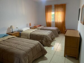 Une chambre avec trois lits, une table de chevet en bois, une lampe et une fenêtre avec des rideaux.