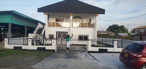A two-story building with a gated entrance, a covered porch, and a staircase leading to the upper level. - 3-bedroom house in quaint Paramaribo with cool AC breeze. (Paramaribo)