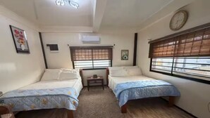Une chambre avec deux lits, une petite table et une fenêtre avec des stores.