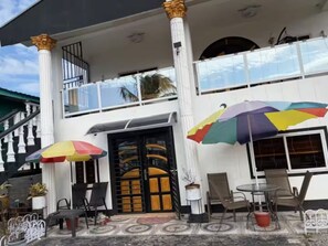 A two-story building with a balcony, outdoor seating area with chairs and tables, and colorful umbrellas. - 3-bedroom house in quaint Paramaribo with cool AC breeze. (Paramaribo)