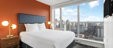 A hotel room with a large bed, a nightstand, a TV, and a city view.