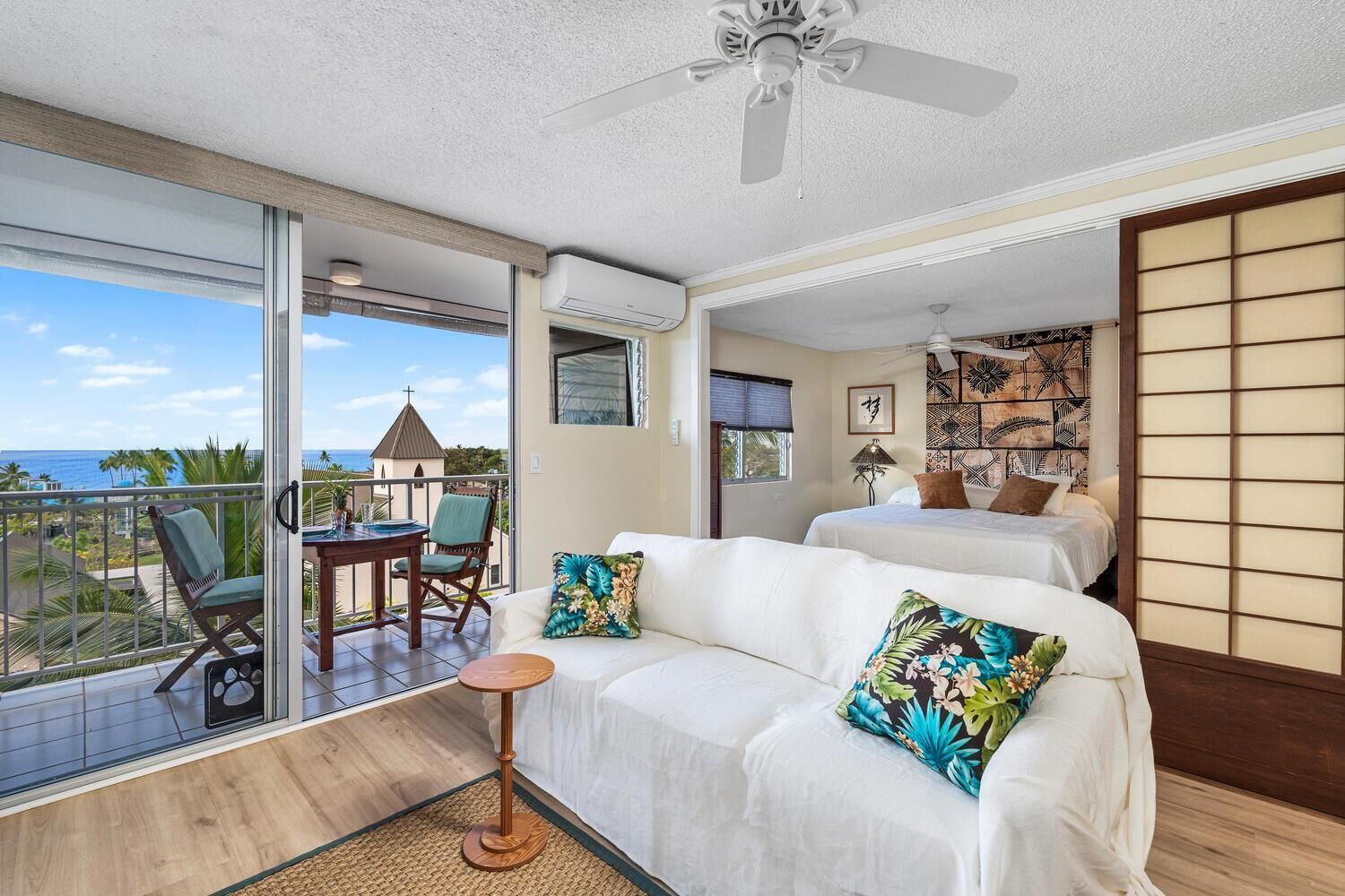 A hotel room with a balcony, a bed, a sofa, and a small table.