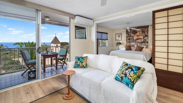 A hotel room with a balcony, a bed, a sofa, and a small table. - Kailua Village#604 (Kailua-Kona)