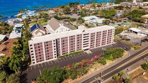 A multi-story hotel with a parking lot and a view of the ocean. - Kailua Village#604 (Kailua-Kona)