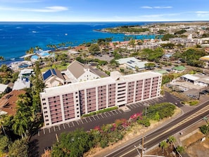 A multi-story hotel with a parking lot and a view of the ocean. - Kailua Village#604 (Kailua-Kona)
