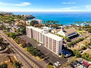 A multi-story hotel with a parking lot and a view of the ocean. - Kailua Village#604 (Kailua-Kona)