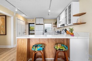 A modern kitchen with white cabinetry, a marble countertop, and wooden stools with floral upholstery. - Kailua Village#604 (Kailua-Kona)