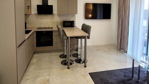 A modern kitchen with a dining area, a flat-screen TV mounted on the wall, and a large window with curtains. - Charming apartment with balcony in the heart of Split (Split)