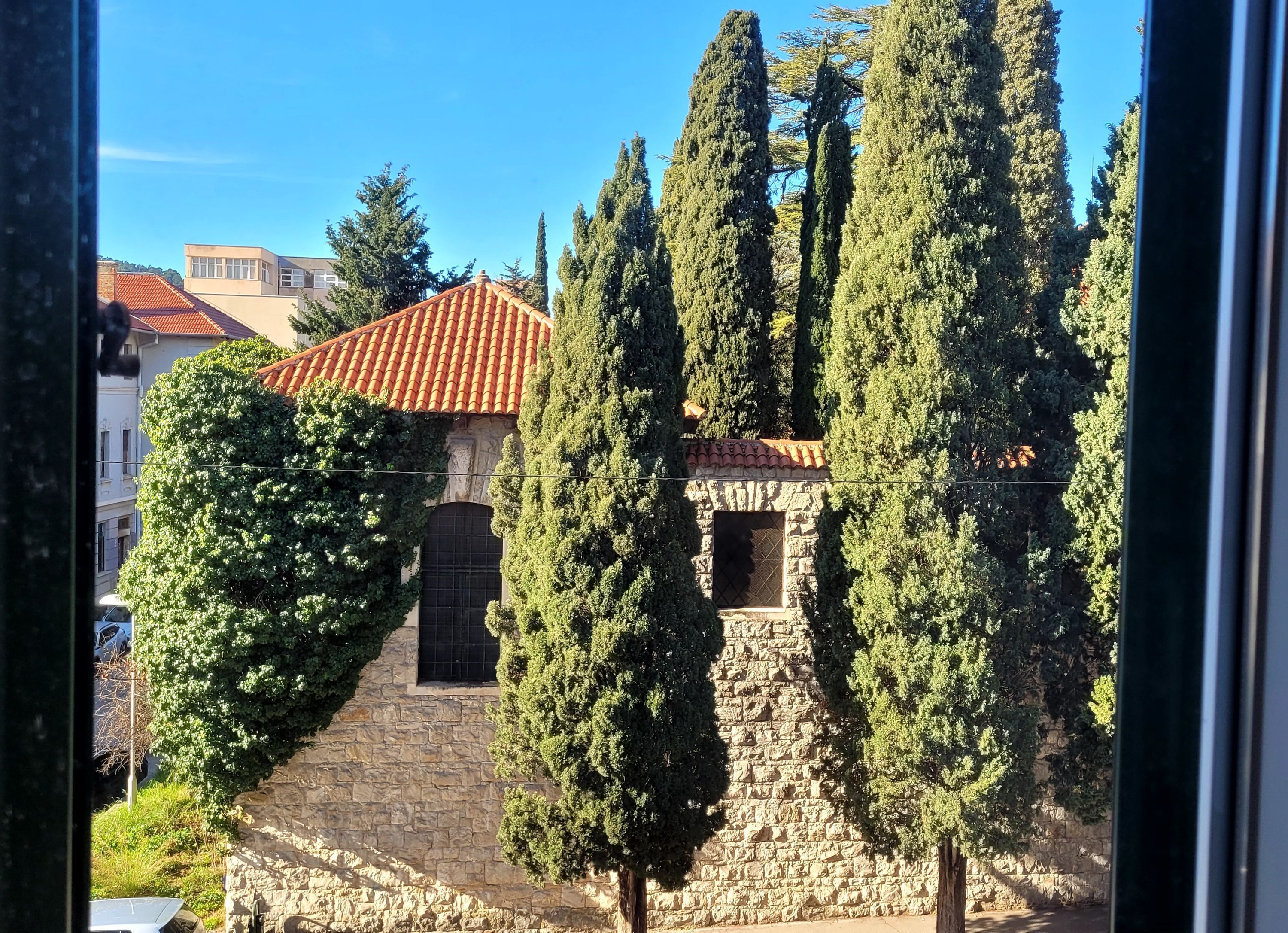 A stone building with a tiled roof, surrounded by tall cypress trees.