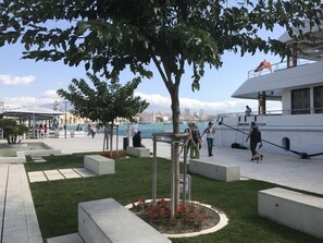 A waterfront promenade with a large tree, seating areas, and a white boat docked nearby. - Charming apartment with balcony in the heart of Split (Split)