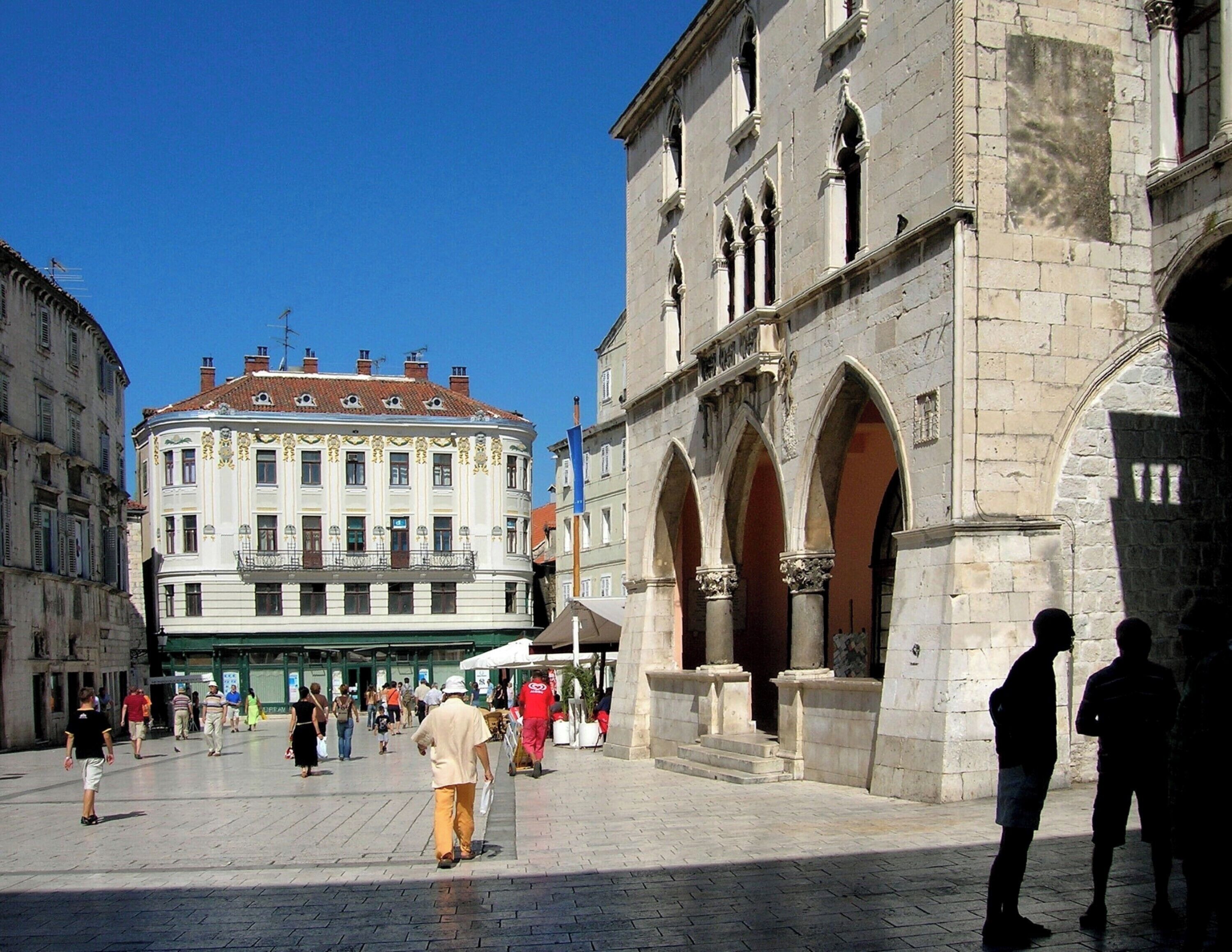A historic square with a prominent building featuring arched windows and a classical facade.