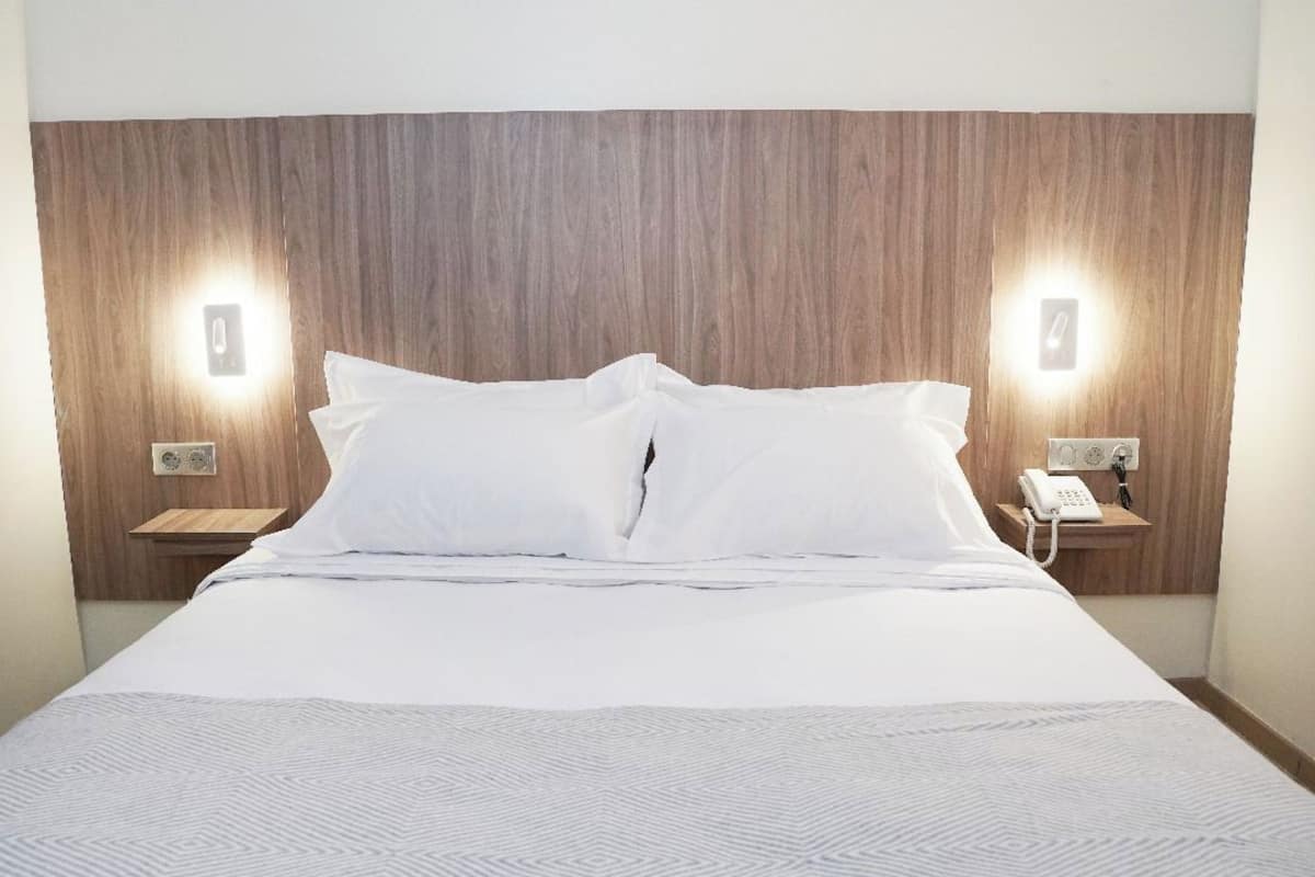 A hotel room with a large bed, wooden headboard, two bedside tables with lamps, and a phone on one of the tables.