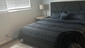 Un dormitorio con cama, mesita de noche, lámpara y ventana con persianas.