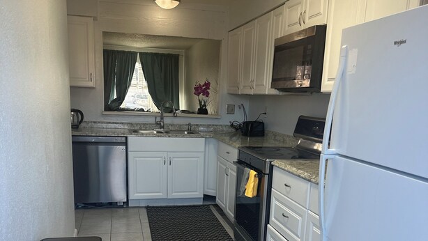 Una cocina compacta con armarios blancos, un refrigerador de acero inoxidable, un horno empotrado y un pequeño cubo de basura.