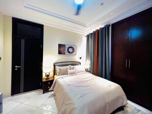 Un dormitorio con cama, mesita de noche, lámpara, una obra de arte en la pared y armario.