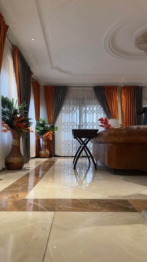 Un salón amplio con un sofá grande de cuero marrón, una mesita de centro y dos jarrones grandes con plantas.