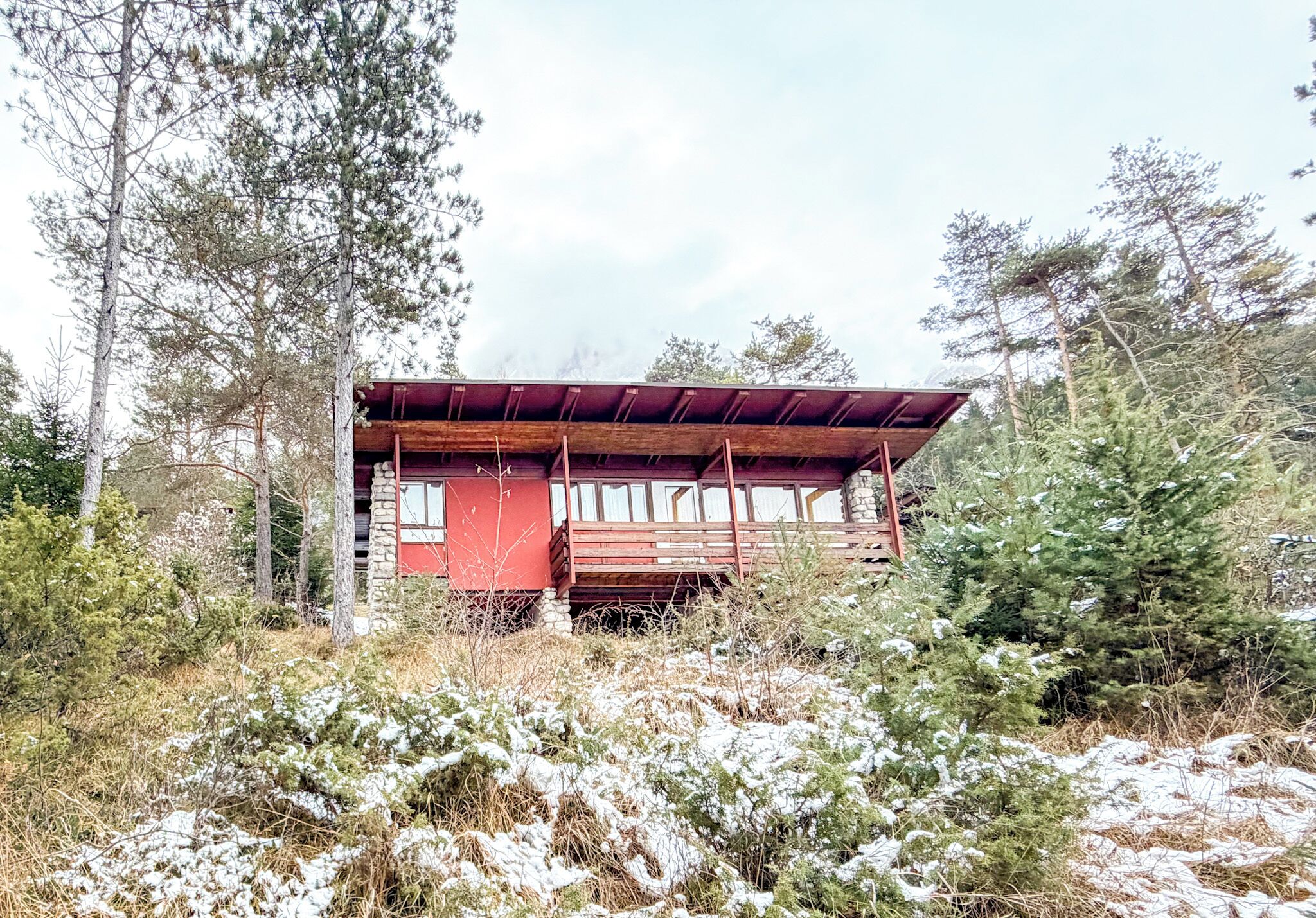 Una cabaña con puerta roja y fachada de madera, rodeada de árboles y nieve.