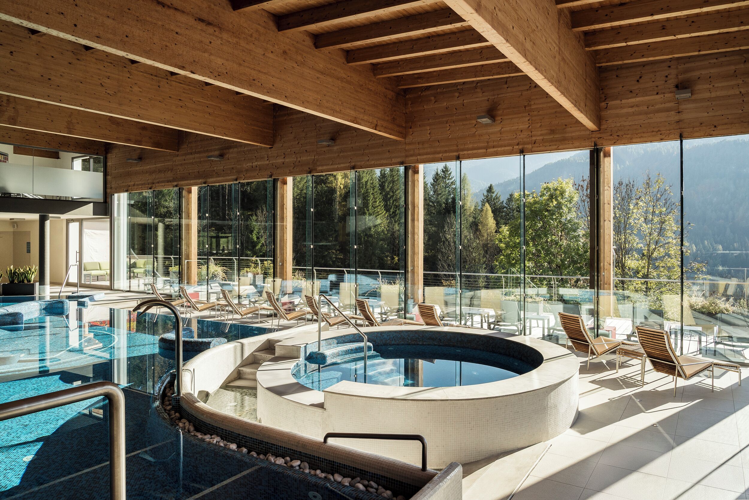 En modern inomhuspool med träbjälkar, glasväggar och solstolar.