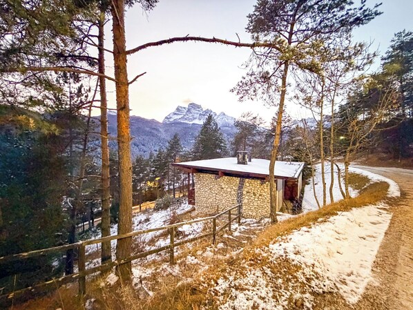 A stone cabin with a metal roof, surrounded by snow-covered ground and trees, with a mountain range in the background. - Panoramic Chalet in the ENI Village near Cortina D'Ampezzo - Spa - Restaurant (Corte)
