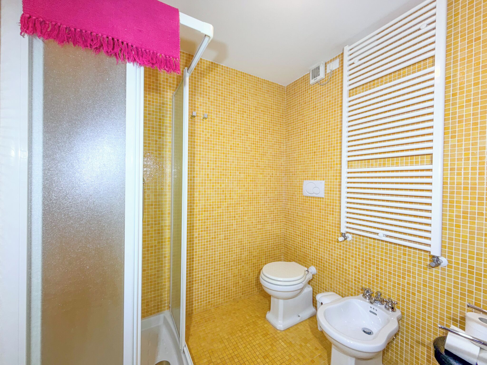 A bathroom with yellow tiled walls, a white toilet, a white sink, and a shower with a glass door.