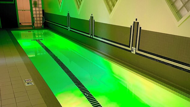 A swimming pool with a green light, tiled walls, and a drain in the center. - Comfortable, clean, and spacious home with heated indoor pool (Green Bay)