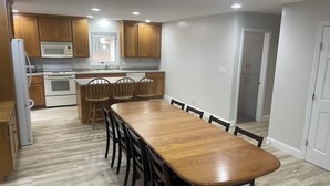 A modern kitchen with wooden cabinets, a white refrigerator, a microwave, and an oven. There is a dining table with chairs and a view of the adjacent living area. - Comfortable, clean, and spacious home with heated indoor pool (Green Bay)