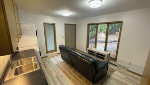 A compact living space with a kitchenette, a black leather sofa, a small wooden cabinet, and a large window offering a view of the outdoors. - Comfortable, clean, and spacious home with heated indoor pool (Green Bay)