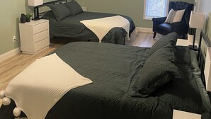 A bedroom with two beds, a chair, a window, and a nightstand with a lamp. - Comfortable, clean, and spacious home with heated indoor pool (Green Bay)