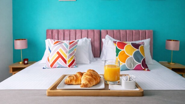 A neatly made bed with a pink headboard, colorful pillows, and a tray with croissants and orange juice. - Brighton Colour Pop House-Sleeps up to 12 (Brighton and Hove)