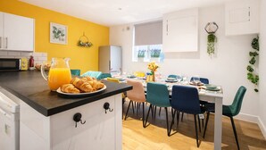 A modern kitchen with a breakfast setup, including croissants and orange juice, and a dining area with a table set for four. - Brighton Colour Pop House-Sleeps up to 12 (Brighton and Hove)