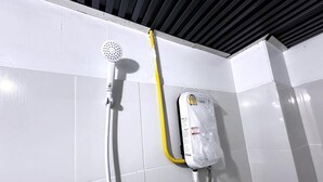 Een doucheruimte met een handdouche en een waterboiler aan de muur.