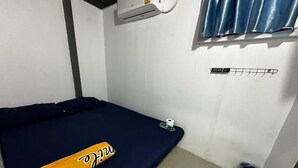 Een kleine kamer met een enkel bed, een donkerblauwe matras, een handdoek en een fles op de vloer.