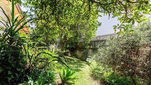 A garden pathway with lush greenery and a stone bridge in the background.
