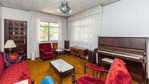A room with a wooden piano, red upholstered furniture, a small table, and a window with curtains.