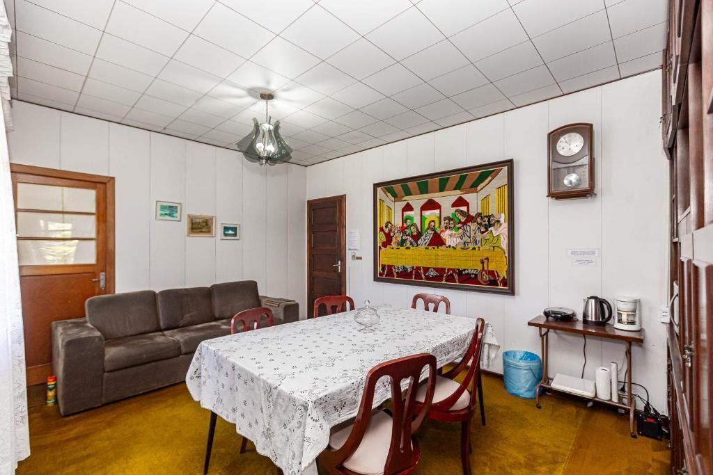 A dining area with a table set for four, a sofa, a clock, and a painting on the wall.