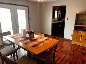 Een eethoek met een houten tafel, stoelen, een vaas met bloemen en een keuken op de achtergrond.