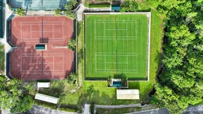 An aerial view of a sports complex with two tennis courts and a football field. - Oasis of Greens & Courts | Car-Free, Quiet Resort (Wesley Chapel)