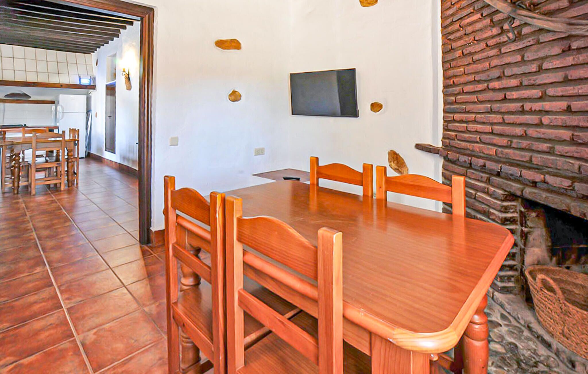 A dining area with a wooden table and chairs, a flat-screen TV mounted on the wall, and a brick fireplace.