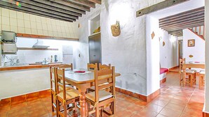 Una cocina con comedor, sillas de madera, piso de baldosas y una escalera que sube a otro nivel.