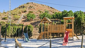 Un parque infantil con un tobogán de madera y una estructura para escalar, rodeado por una cerca de cuerda.